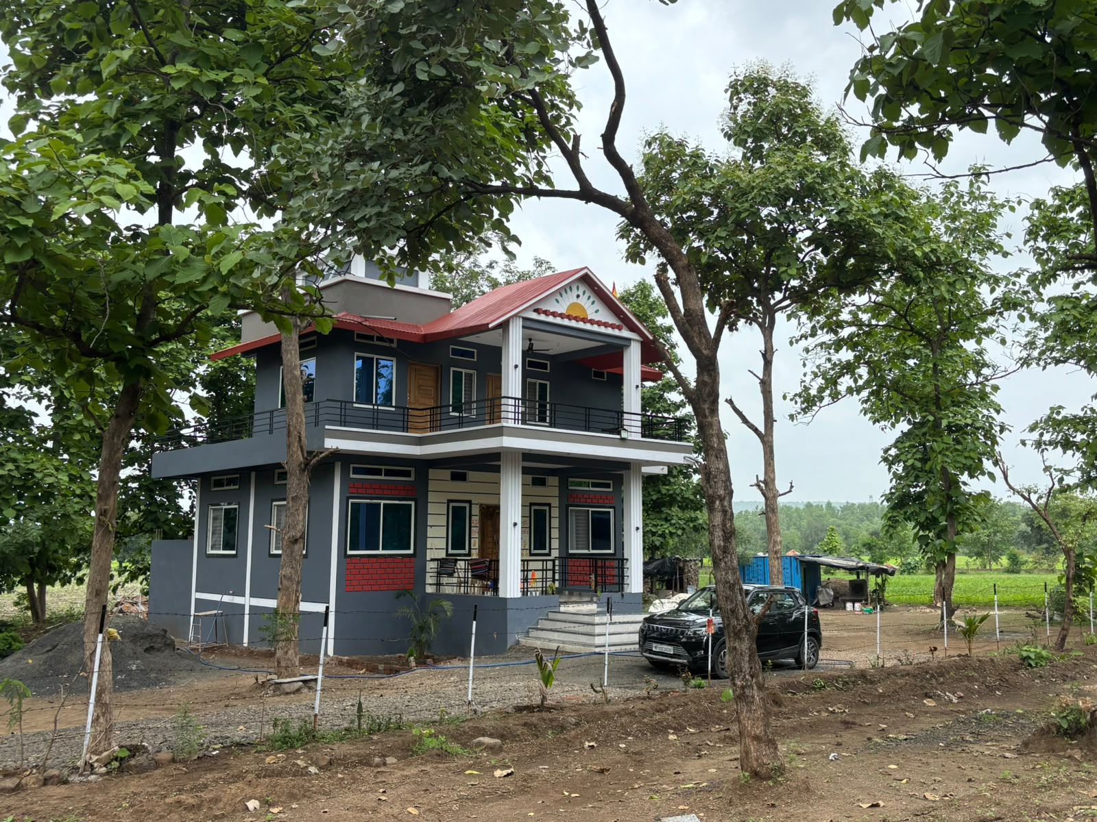 Deepti Ecostays farmhouse — a grey two-storey home with a red roof, set among tall teak trees